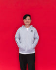 A man wearing an Adult Carey Mickey Hoodie - Grey hoodie with a small black-and-white chest graphic on the front.
