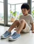 Child wearing blue shoes sitting on a floor with large windows in the background