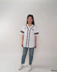 Mother wearing a white baseball jersey with black accents and blue jeans on a plain background