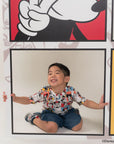 Child in pop comic mickey tee in front of a large Mickey Mouse poster