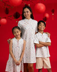 Three kids in matching Elly Zodiac Mahjong outfits against a red background.