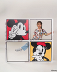 Child wearing pop comic mickey tee and holding up four framed Disney character posters on a white wall.
