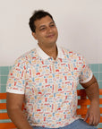 Men's Childhood Games Polo Tee by Elly - Front view of man in signature print sitting on a bench.