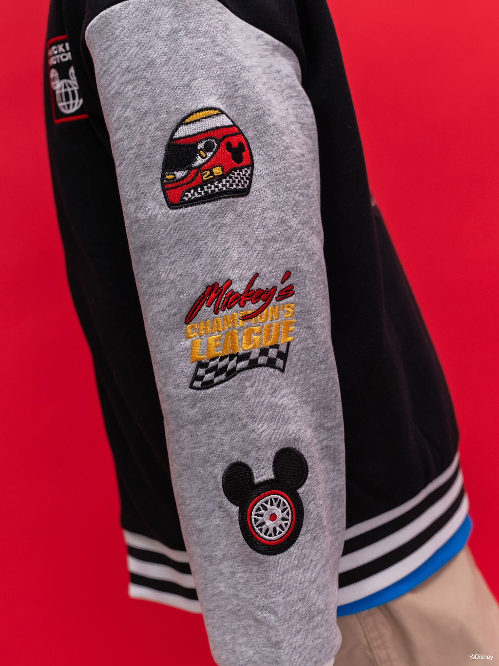 Close-up of a Bomber jacket Mickey 28 with racing-themed embroidered patches, including a helmet patch, 'Mickey's Speedway League' text, and a Mickey Mouse wheel patch.