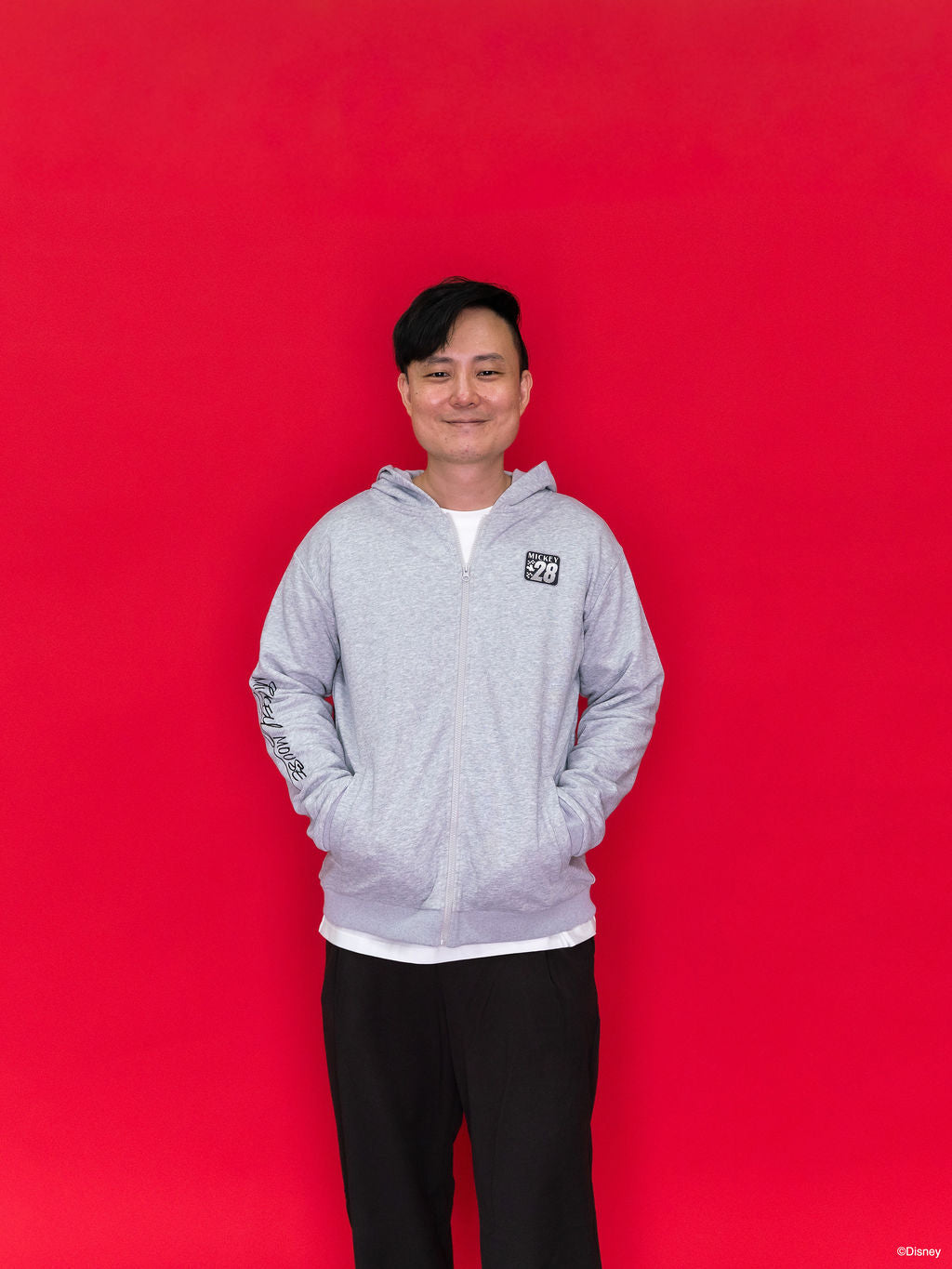 A man wearing an Adult Carey Mickey Hoodie - Grey hoodie with a small black-and-white chest graphic on the front.