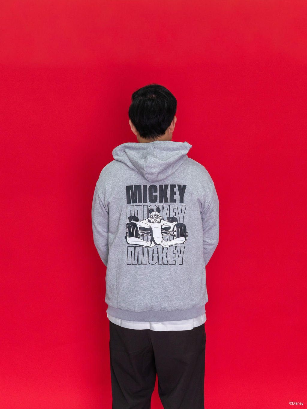 An adult wearing an Adult Carey Mickey Hoodie - Grey hoodie with a large Mickey Mouse in a racing car graphic on the back