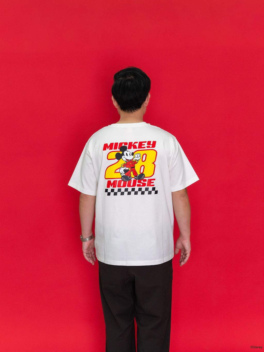 A man viewed from behind wearing a white Mickey Mouse graphic T-shirt with a large red, yellow, and black back print.