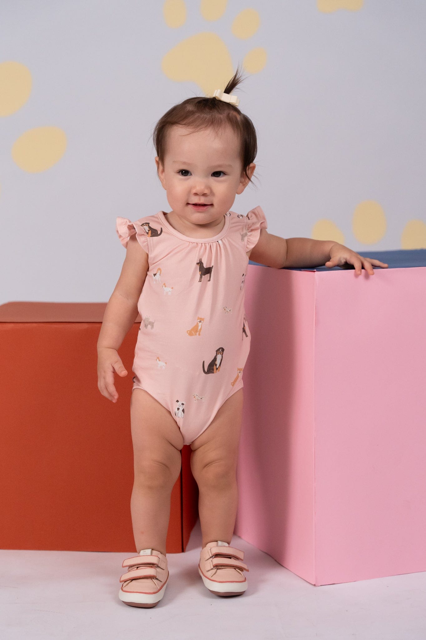 Baby girl in dog-print bodysuit, standing.
