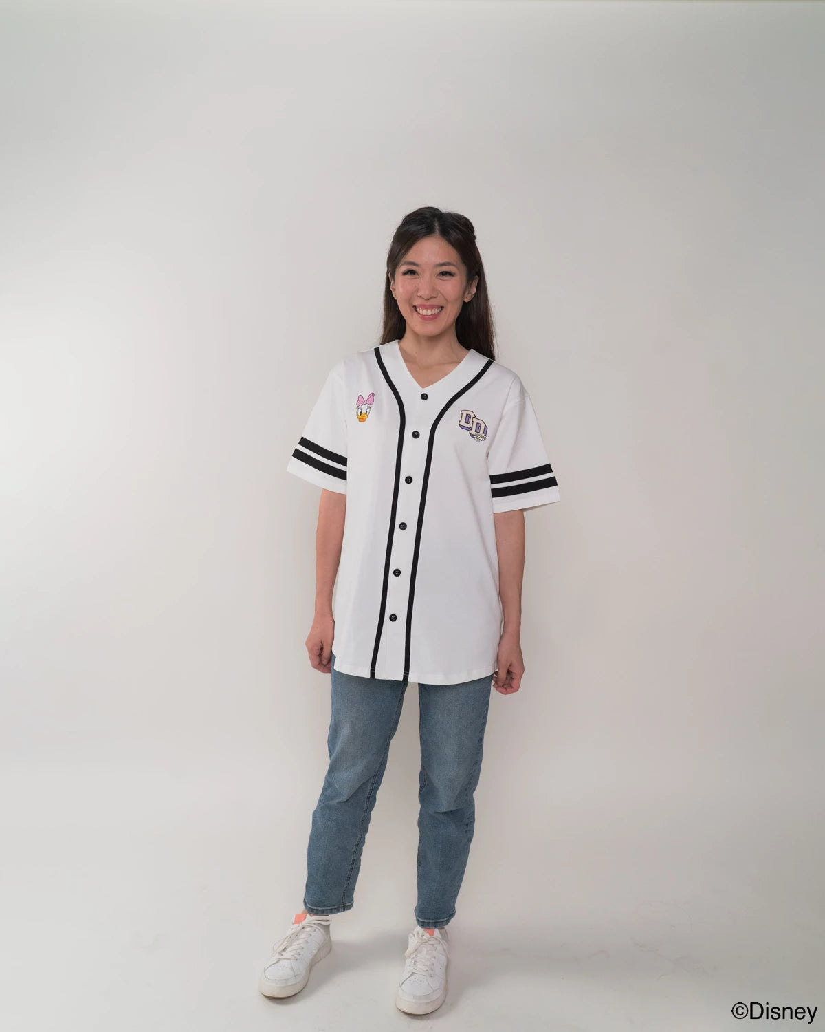 Mother wearing a white baseball jersey with black accents and blue jeans on a plain background