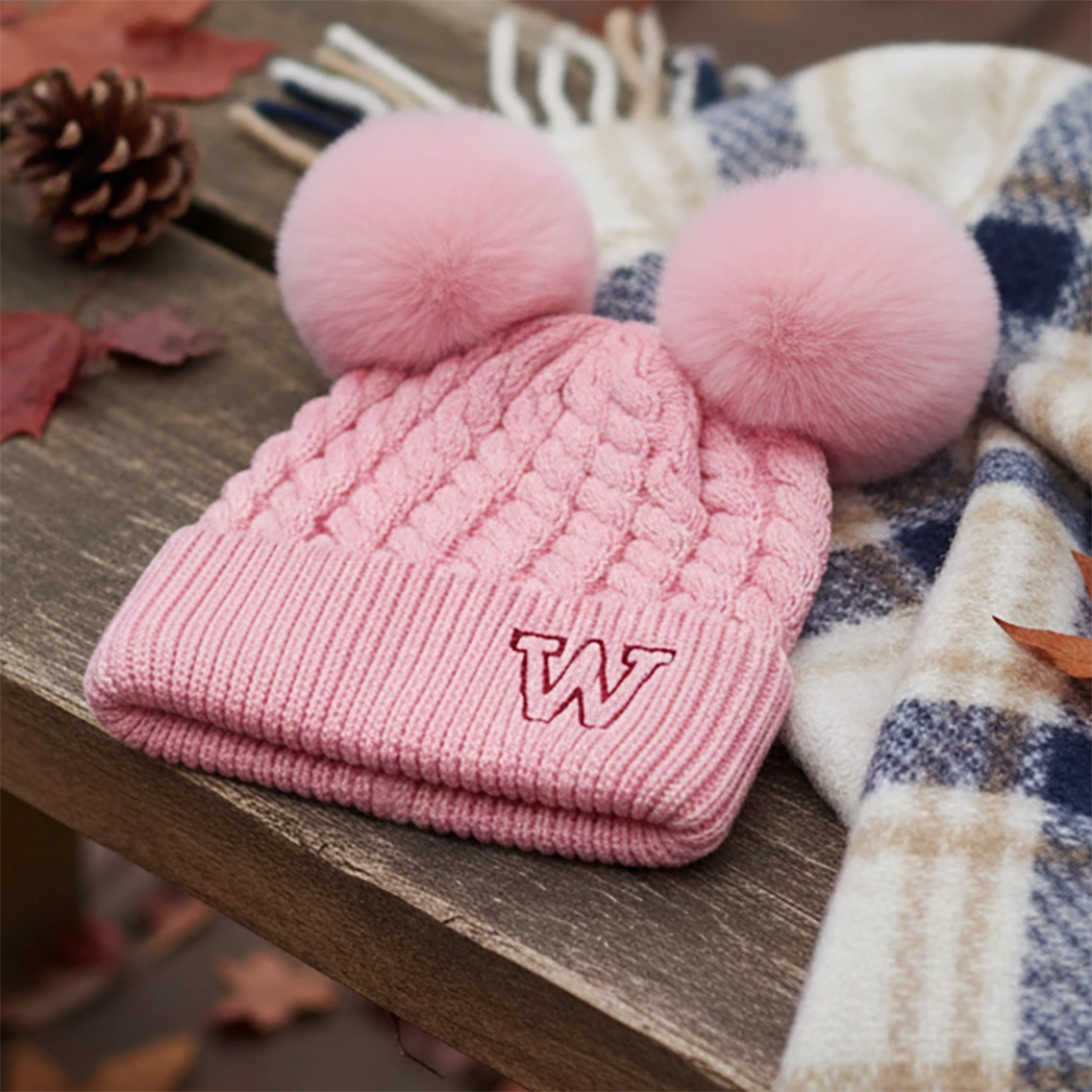 Pink knitted beanie with double pom-poms on an autumn table
