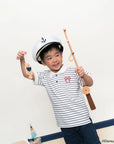 Child wearing a sailor hat and polo tee in stripe sailor mickey holding a toy boat and oar.