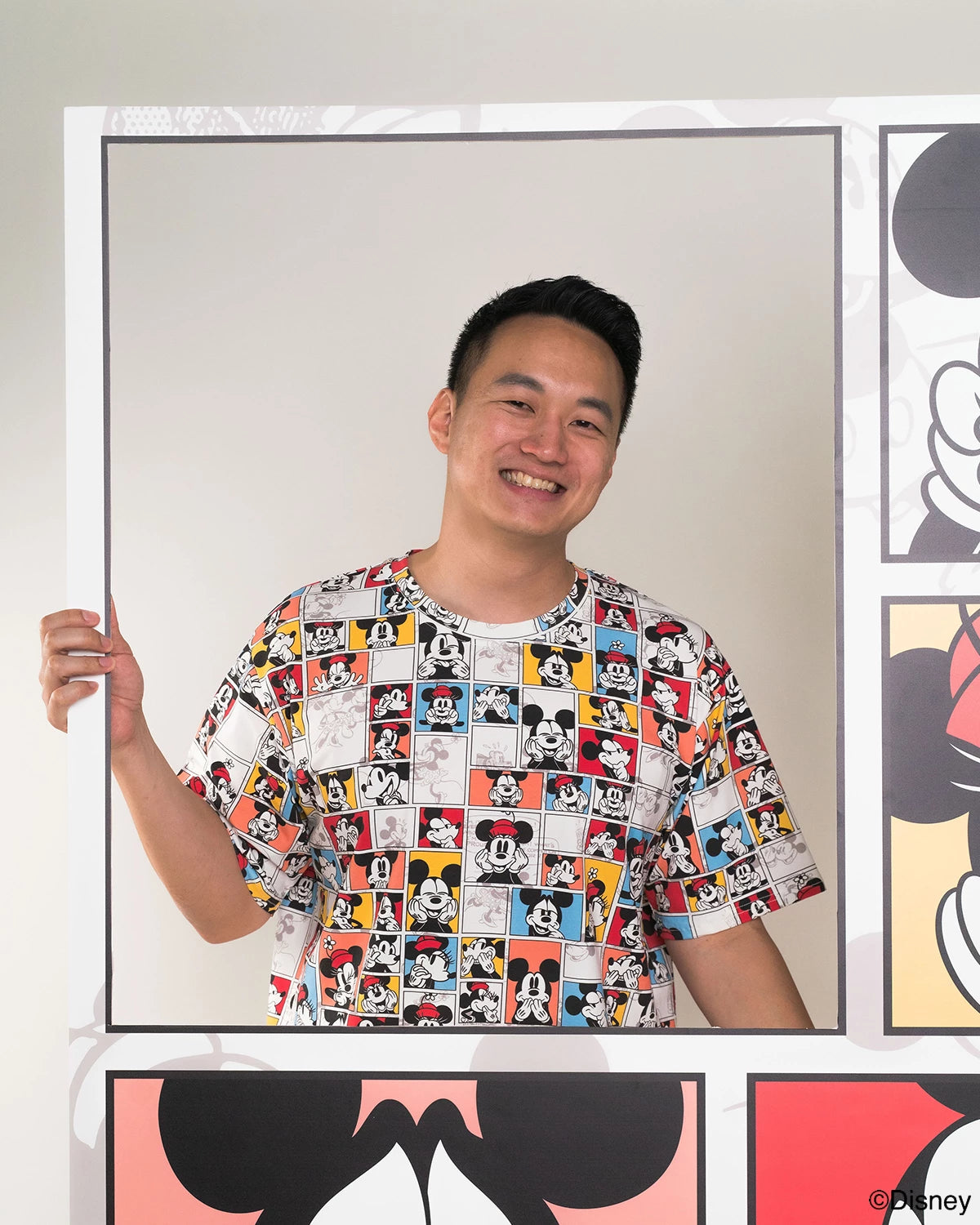 Person wearing adult pop comic mickey tee standing in front of Disney-themed artwork.