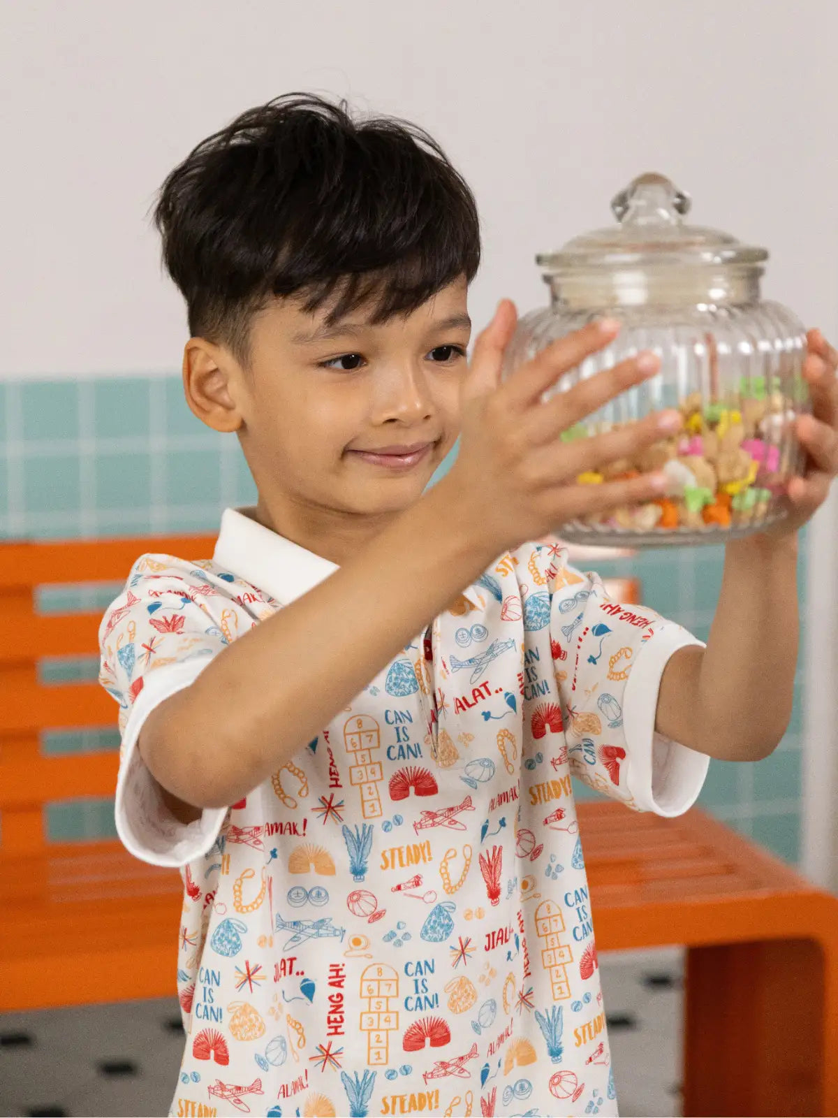 Boy holding a candy jar wearing the Childhood Games Polo Tee by Elly.