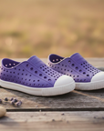 Purple native kids shoes with white soles on a wooden surface