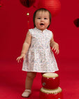 Baby girl wearing Elly Kira Onesie in Zodiac Mahjong print standing by a red drum.