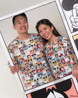 Two people wearing matching adult pop comic mickey tee standing next to a large poster with Mickey Mouse designs.