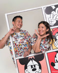 Two people wearing matching adult pop comic mickey tee standing next to a large poster with Mickey Mouse designs.