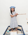 Child in sailor mickey stripes polo dress and sailor hat standing in a toy boat with a white background