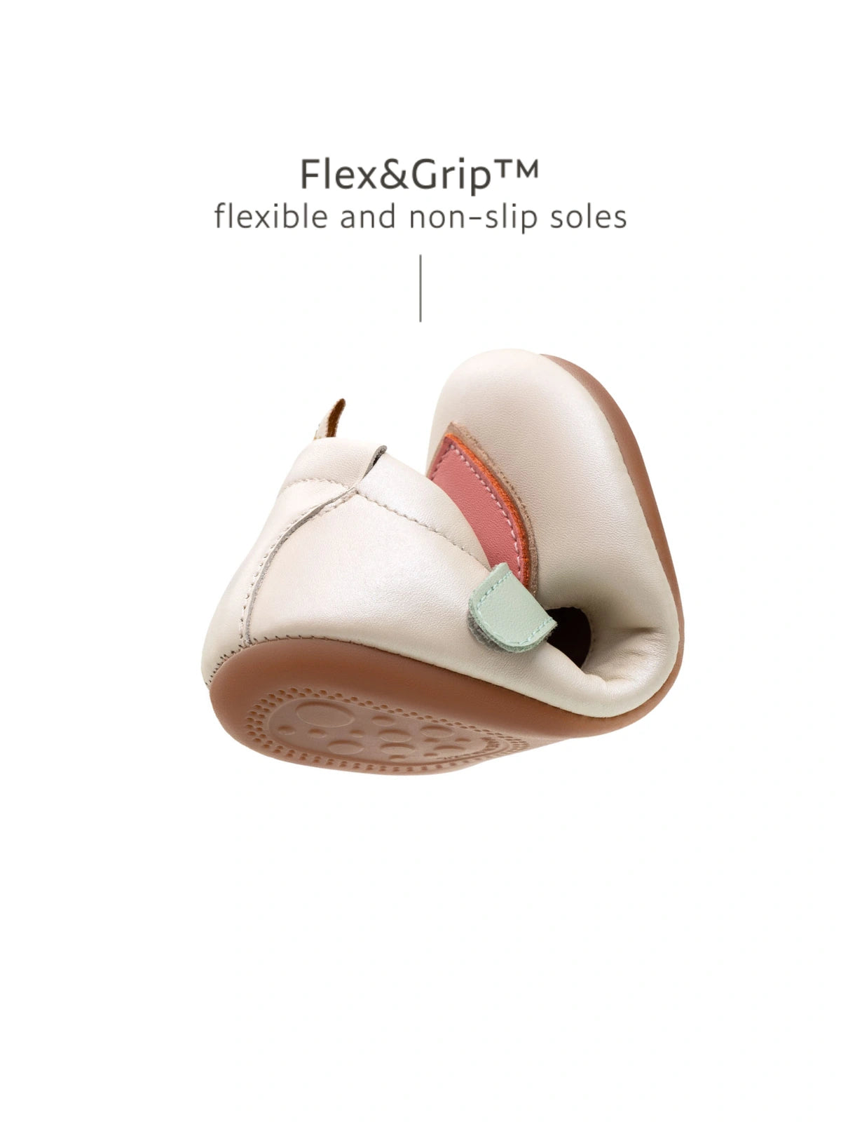 A white leather baby shoe with a pink heart being folded to show the flexible, non-slip rubber sole for first steps.