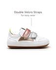 Side view of white and metallic baby sneakers highlighting the adjustable double velcro straps for a secure fit.